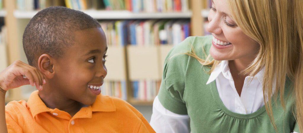 Kindergarten teacher helping student with reading skills smiling looking at each other.